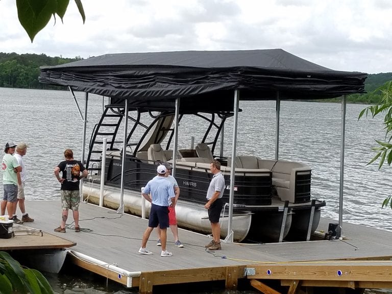 People on a dock beside a pontoon boat covered by a Touchless Automatic Boat Cover, enjoying a sunny day.