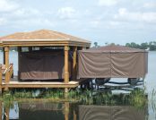 Two docked pontoon boats fully covered by Touchless Covers®; left boat under a roofed boat house, right boat elevated above water