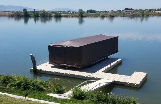 Touchless Boat Cover shielding a docked pontoon boat on a peaceful lake