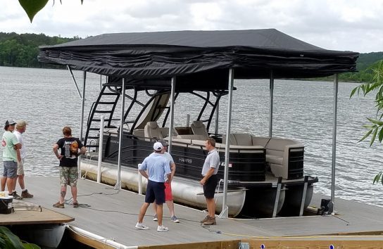 People on a dock beside a pontoon boat covered by a Touchless Automatic Boat Cover, enjoying a sunny day.