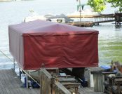 Text: Docked pontoon boat fully protected by a Touchless Automatic Boat Cover on a calm lake
