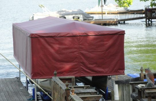 Text: Docked pontoon boat fully protected by a Touchless Automatic Boat Cover on a calm lake