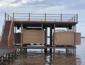 Touchless Boat Covers pitched on a dock, with two pontoon boats fully covered, surrounded by calm waters.