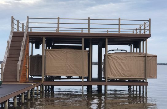 Touchless Boat Covers pitched on a dock, with two pontoon boats fully covered, surrounded by calm waters.