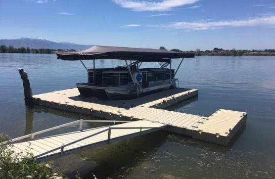 Touchless Boat Cover folded open over a docked pontoon boat on a lake
