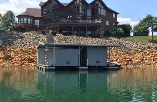 Two pontoon boats docked in front of a mansion, fully covered by Touchless Automatic Boat Covers