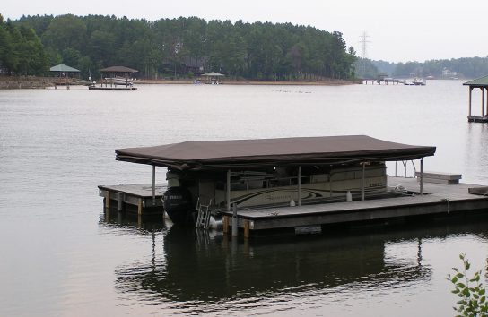 Pontoon boat docked with Touchless Boat Cover retracted overhead
