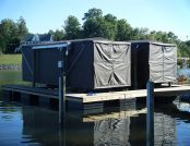 Ski boat and wake boat docked on a calm lake, fully covered by dark gray Touchless Automatic Boat Covers.